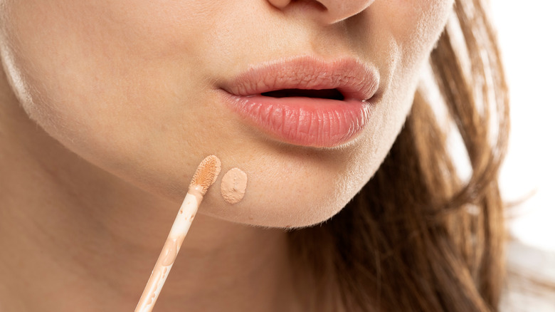 Woman applying concealer on her chin