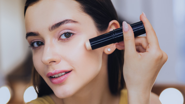 Woman applying concealer stick