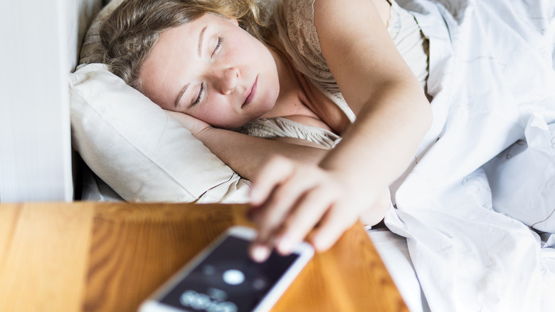 woman hitting phone snooze button