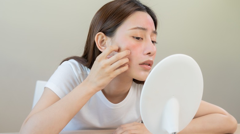 Woman examines skin redness in mirror