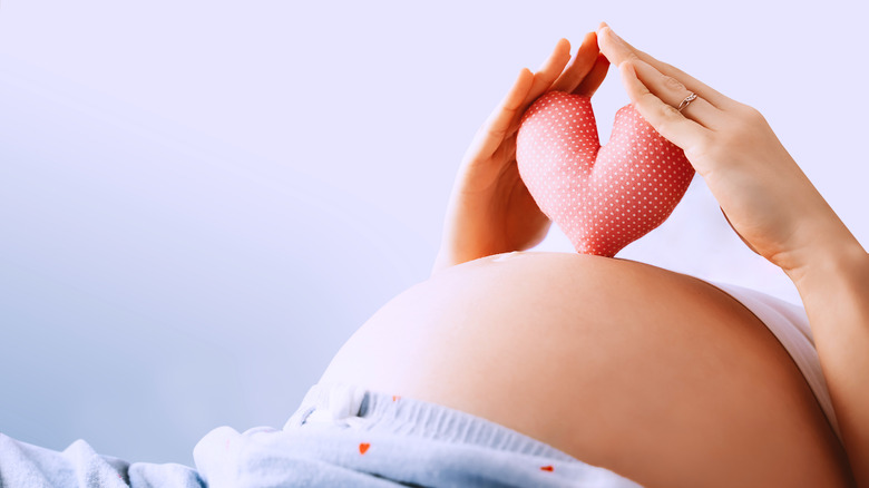 Pregnant person holding heart shape on belly