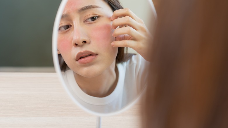 A woman looking at her red face in a mirror