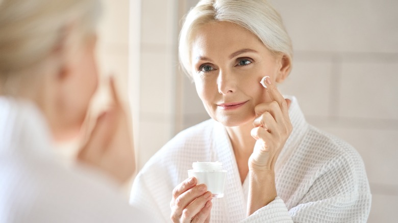 A blonde woman applying face cream