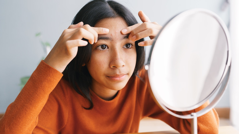 A teenager looking at her acne in the mirror