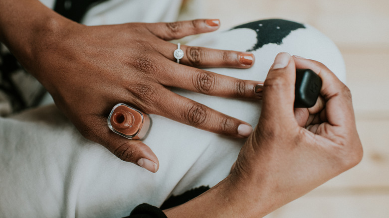 Person wearing an engagement ring painting their nails mocha brown