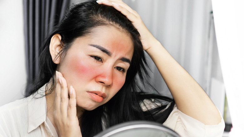 Woman examines facial redness in mirror