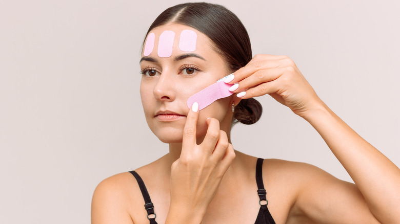 A woman applies colored face tape to her face