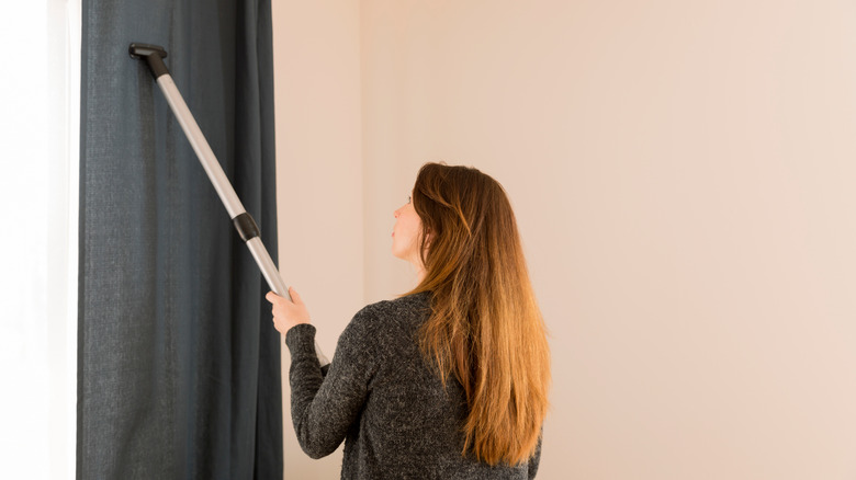 Young woman vacuming curtains