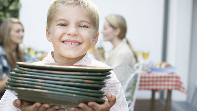 young boy holding stack of plates