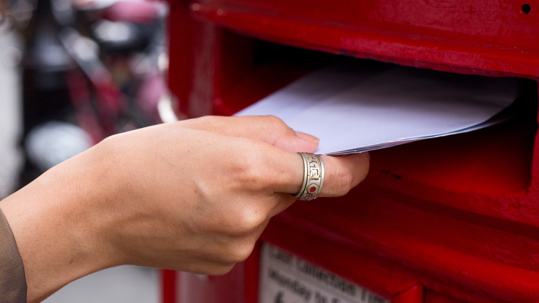 hand putting letters into red mailbox