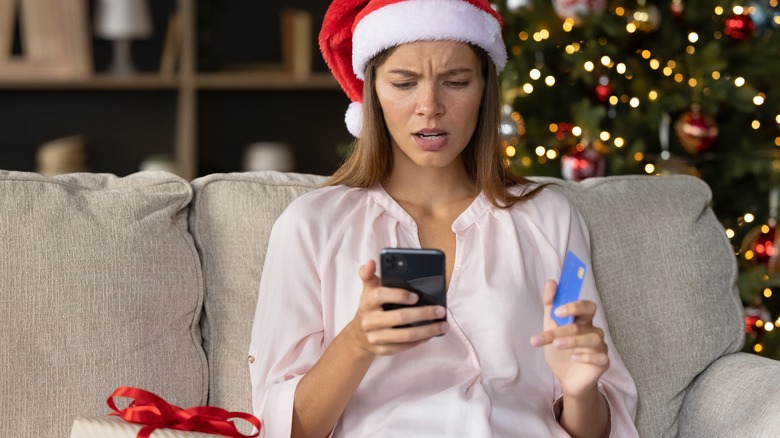 Woman in Santa's hat holding credit card looking concerned