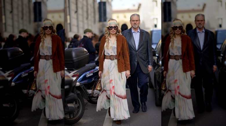 A woman wearing a flowing multi-colored maxi with a tan suede fringed jacket and belt