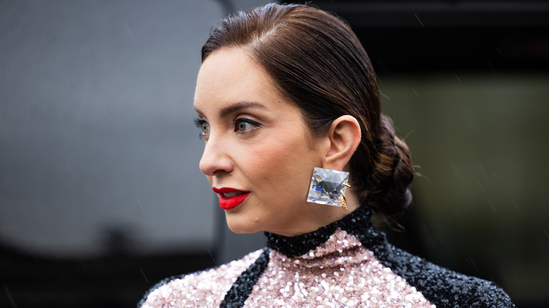 woman wearing huge jewel earrings and a sequined turtle-neck top with red lips and eyeliner.