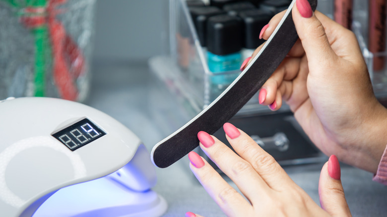 Someone doing their own pink gel manicure at home, using a nail file.