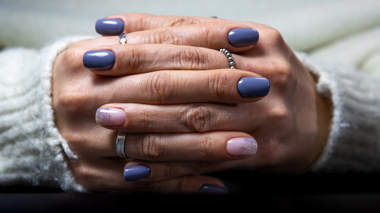 Hands crossed with a purple manicure, including a glittery accent nail.