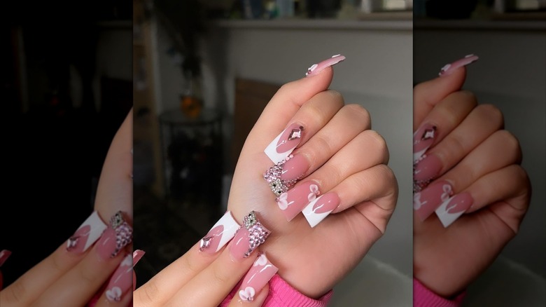 A hand showing flared French nails with bling and floral designs.