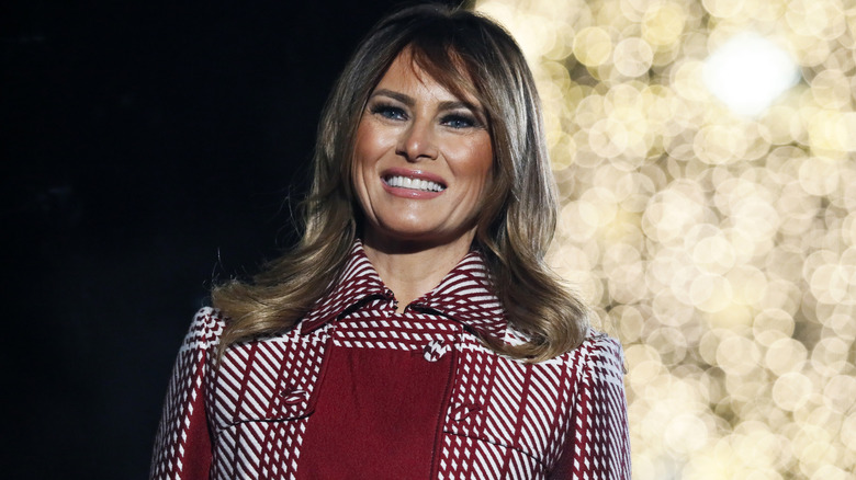 Melania Trump smiling in a plaid red and white coat.