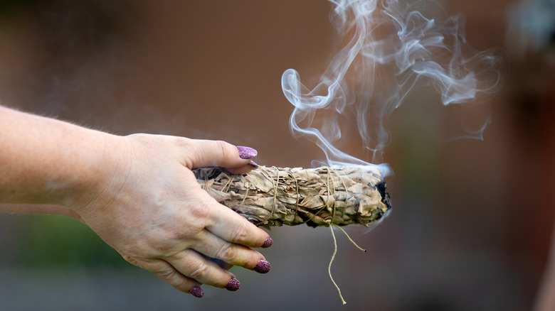 Hand holding a smoking sage bundle