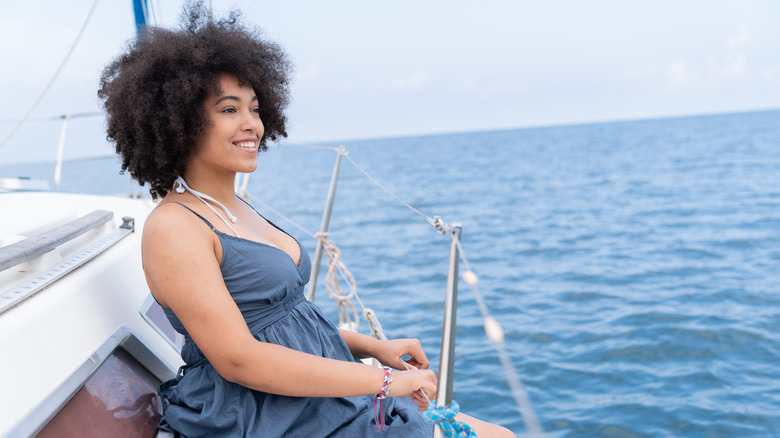 A woman wearing a simple beach dress over her bikini while sitting on a ship.