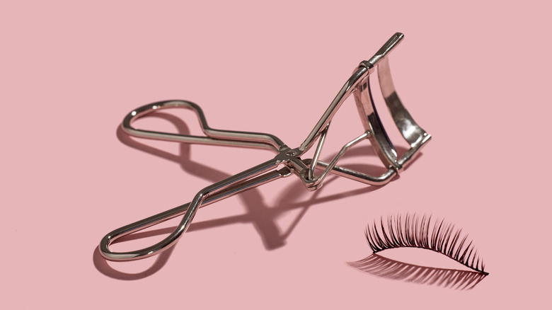 eyelash curler and lashes on pink background