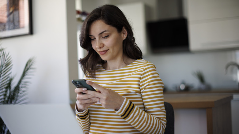 Woman holding mobile phone in front of laptop screen