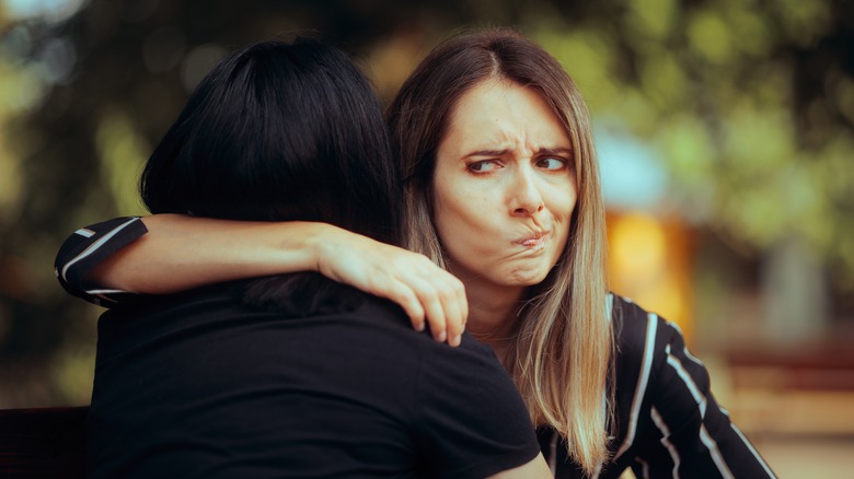 Annoyed woman giving friend fake hug