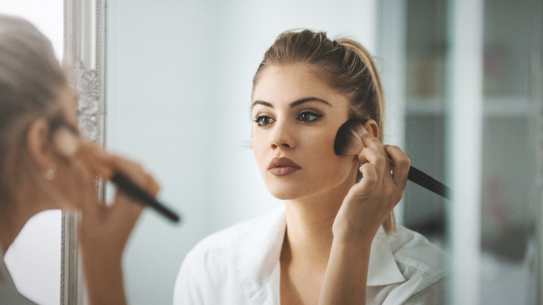 Woman applying blush in mirror