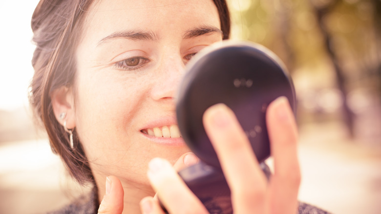 Woman looking at face in compact mirror