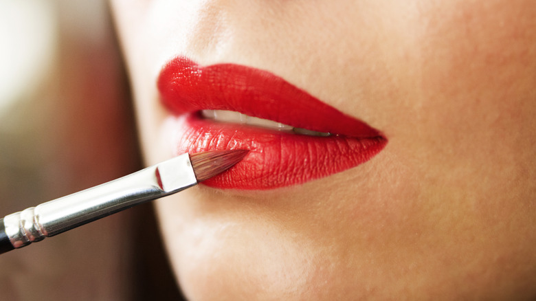 applying red lipstick with lip brush