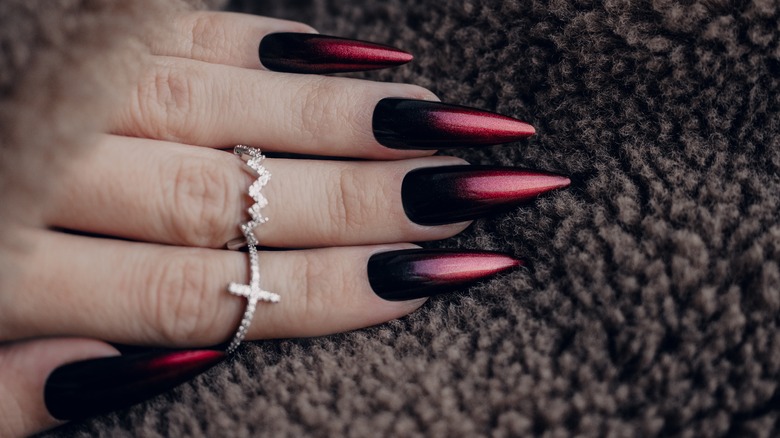 Pointy red and black manicure against brown material