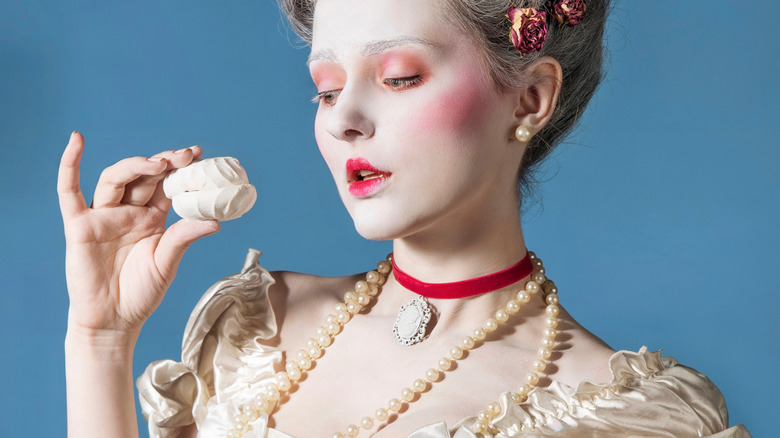 woman in Victorian style makeup and corset dress styled with pearls staring at a pastry