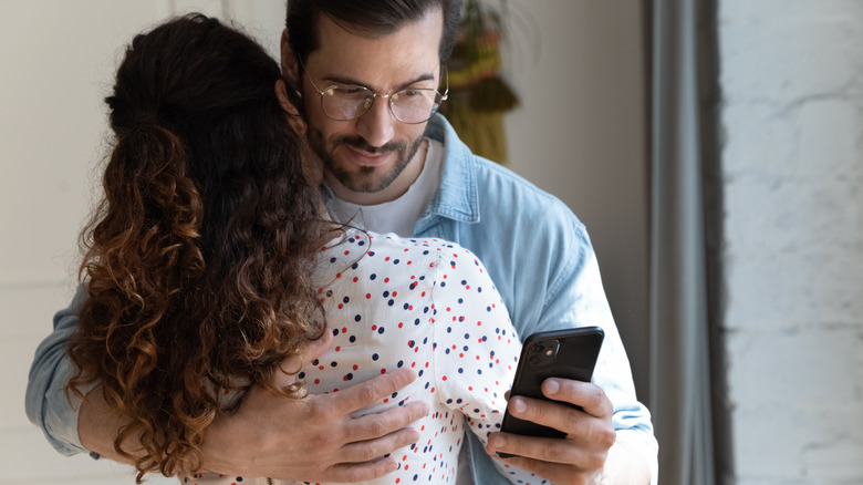 man checking phone hugging partner