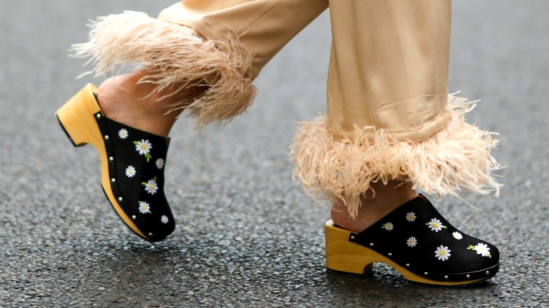 A pair of black clogs with daisy embroidery.