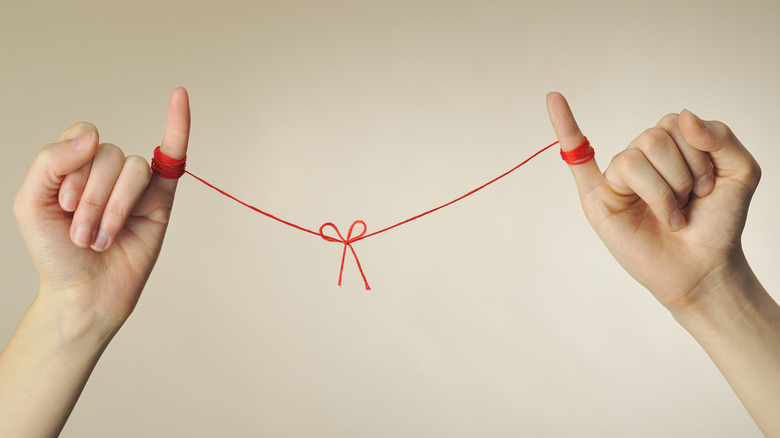 Two hands tied together with red string.