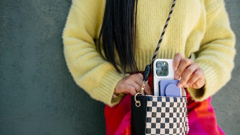 Person in a yellow sweater removing a phone from a black and white checkered purse