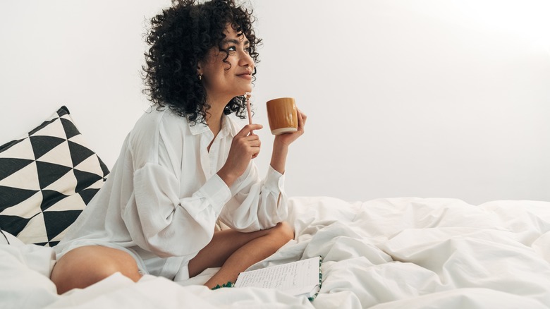 Smiling woman journaling with coffee in bed