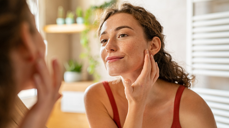 smiling woman examining face in mirror