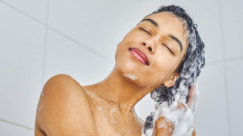 A woman lathering her hair with shampoo in the shower