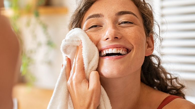 female pat her face with a towel looking into the mirror