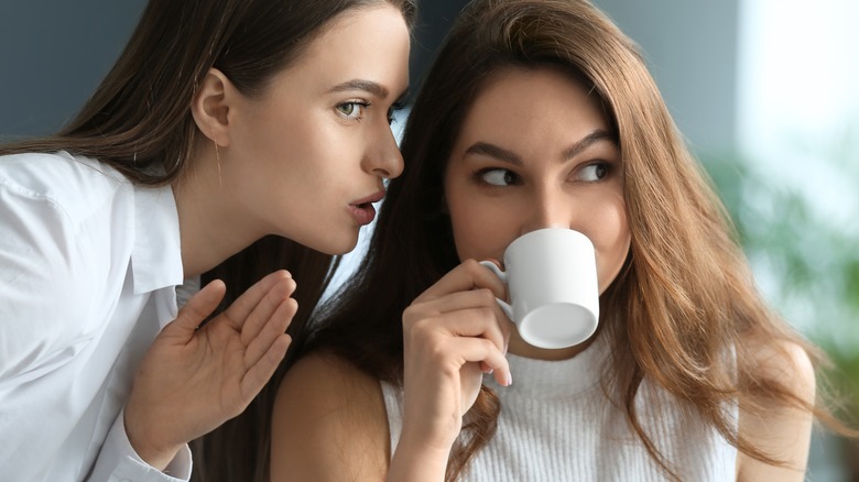 Woman whispers to woman drinking tea