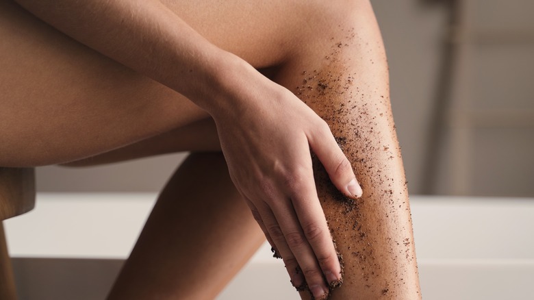 woman exfoliating calf with brown scrub