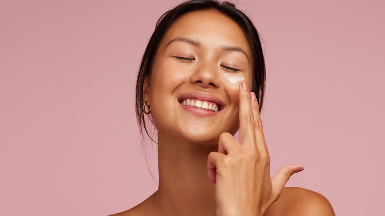 smiling woman applying cream against pink background