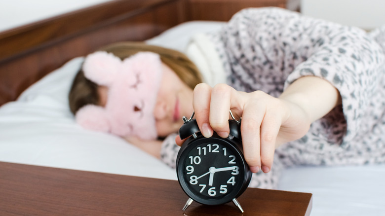 woman in bed touching alarm clock