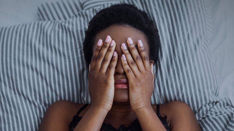 woman covering eyes in bed