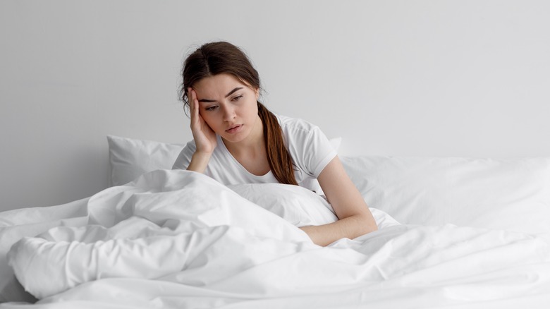 Woman holding head in bed