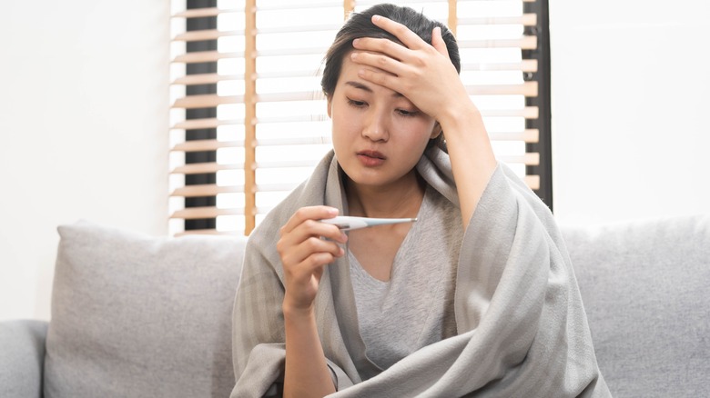 Sick woman with blanket and thermometer 