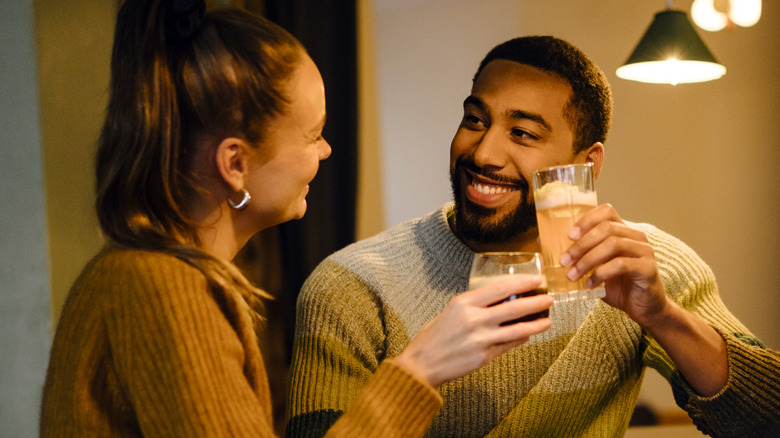 Man smiling at woman as they tap drink glasses