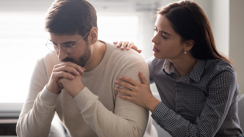 Woman grasping man's shoulder apologetically 