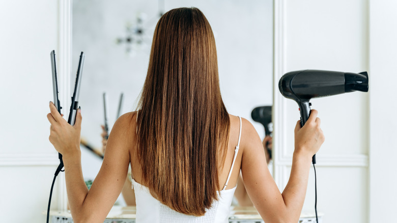 Woman holding straightener and blowdryer