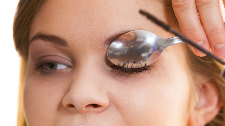 Woman using spoon to apply mascara